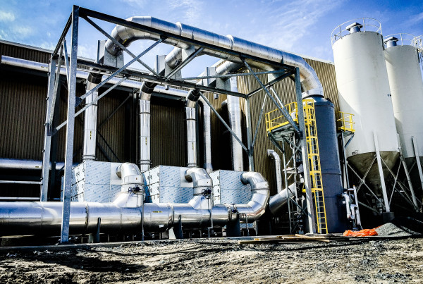 Stainless steel ductwork and odor control units outside a biosolids facility, with two white storage silos beside them