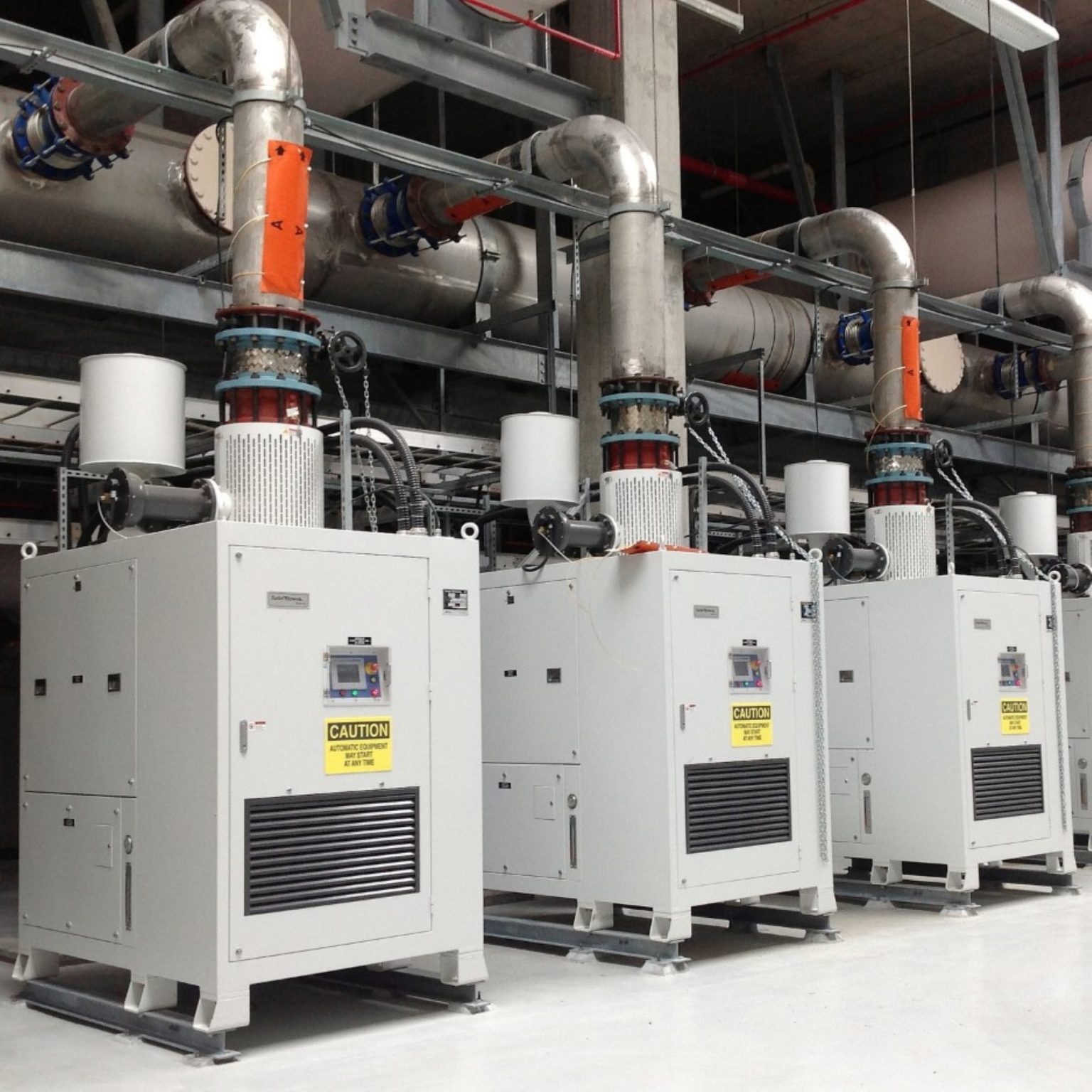 Row of APG-Neuros turbo blower enclosures with touchscreen control panels and overhead discharge piping in a blower room