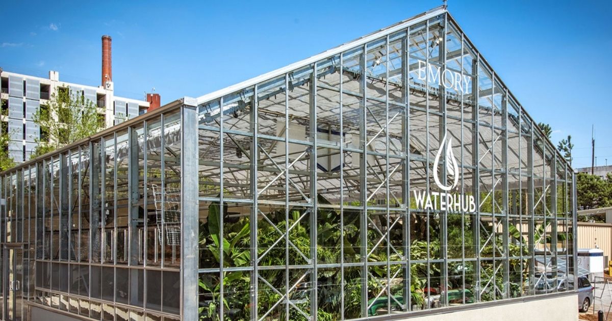 Emory University WaterHub by H2O Innovation, a glass greenhouse-style water reclamation facility filled with plants, with campus buildings behind